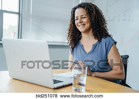 Mixed race businesswoman smiling at laptop View Large Photo Image Stock Photo - Mixed race businesswoman smiling at laptop. Fotosearch