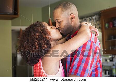 Stock Image - Mixed race couple kissing in kitchen. Fotosearch