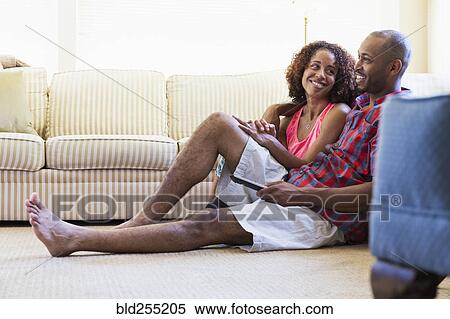 Stock Photography - Mixed race couple sitting on floor watching television. Fotosearch
