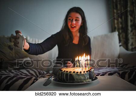 Stock Image - Mixed race girl posing for cell phone selfie with birthday cake. Fotosearch