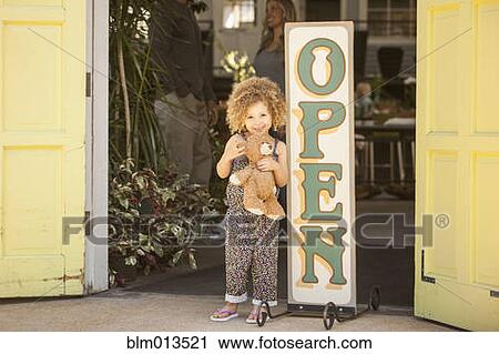 Stock Image - Mixed race girl standing near flower shop open sign. Fotosearch