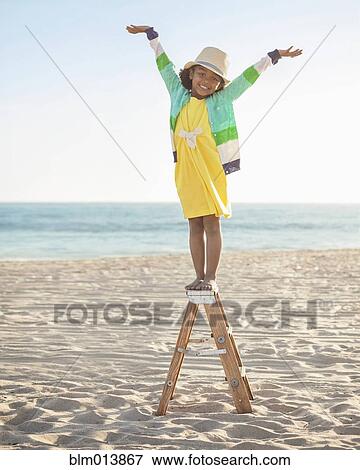 Stock Photo - Mixed race girl standing on ladder on beach. Fotosearch