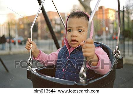 Picture - Mixed race girl swinging in playground. Fotosearch