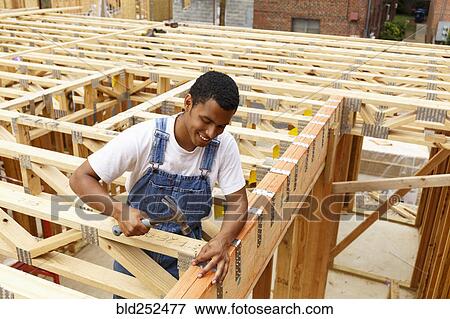 Stock Photo - Mixed race man hammering nail at construction site. Fotosearch