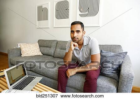 Stock Photo - Mixed race man relaxing on sofa near laptop. Fotosearch