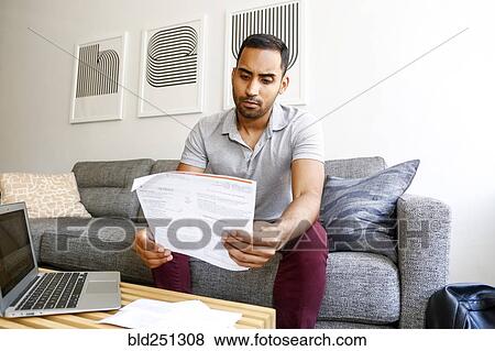 Mixed race man sitting on sofa reading paperwork View Large Photo Image Stock Photo - Mixed race man sitting on sofa reading paperwork. Fotosearch