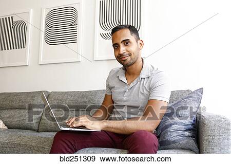Mixed race man sitting on sofa using laptop View Large Photo Image Stock Photo - Mixed race man sitting on sofa using laptop. Fotosearch