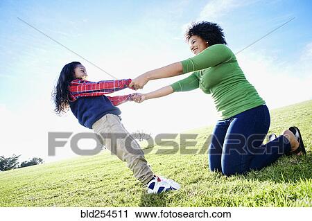 Stock Image - Mixed race mother and daughter playing in grass. Fotosearch