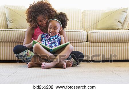 Mixed race mother and daughter reading book on floor near sofa View Large Photo Image Stock Image - Mixed race mother and daughter reading book on floor near sofa. Fotosearch