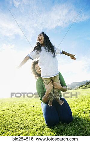 Stock Photograph - Mixed race mother holding daughter pretending to be airplane. Fotosearch