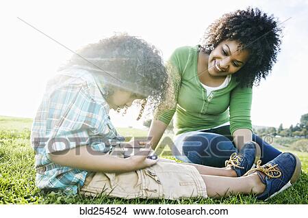 Mixed race mother watching son use cell phone in grass View Large Photo Image Picture - Mixed race mother watching son use cell phone in grass. Fotosearch