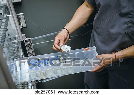 Stock Image - Mixed race nurse examining vial of medicine. Fotosearch