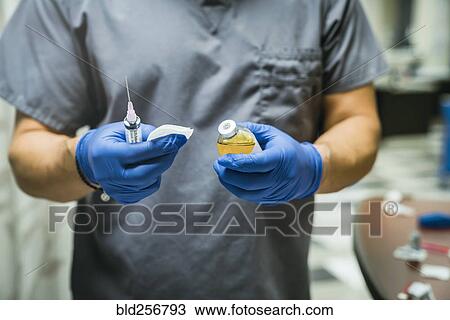 Stock Image - Mixed race nurse wearing rubber-gloves holding medicine and needle. Fotosearch
