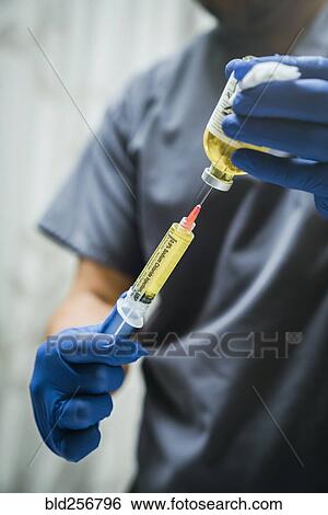 Stock Photograph - Mixed race nurse wearing rubber-gloves holding medicine and needle. Fotosearch