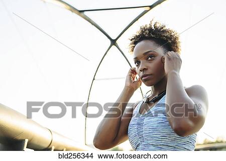 Picture - Mixed Race woman adjust earbuds. Fotosearch