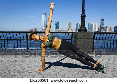 Stock Image - Mixed race woman balancing on arm at waterfront. Fotosearch