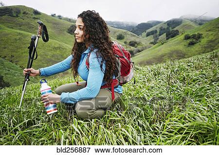 Mixed race woman crouching in grass holding walking sticks and bottle View Large Photo Image Stock Photo - Mixed race woman crouching in grass holding walking sticks and bottle. Fotosearch