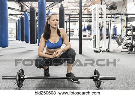 Stock Photo - Mixed race woman crouching near barbell in gymnasium. Fotosearch