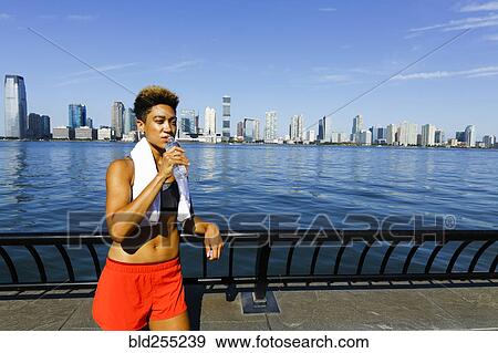 Mixed race woman drinking water from bottle at waterfront View Large Photo Image Stock Photo - Mixed race woman drinking water from bottle at waterfront. Fotosearch