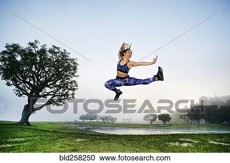 Stock Image - Mixed race woman exercising and jumping near lake. Fotosearch