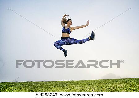 Stock Photo - Mixed race woman exercising and jumping in field. Fotosearch