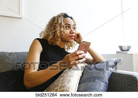Mixed race woman laying on sofa holding cell phone View Large Photo Image Picture - Mixed race woman laying on sofa holding cell phone. Fotosearch