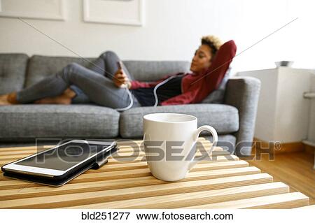 Stock Photo - Mixed race woman laying on sofa listening to earbuds. Fotosearch