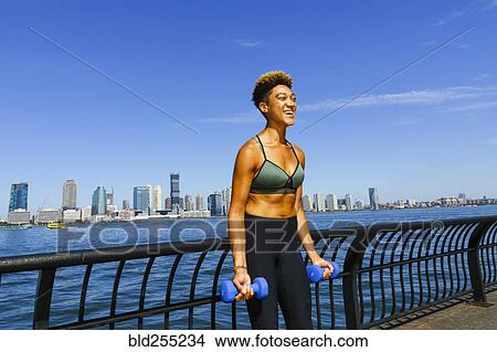 Picture - Mixed race woman lifting dumbbells at waterfront. Fotosearch