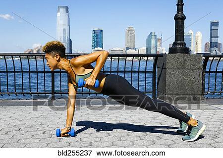 Stock Photo - Mixed race woman lifting dumbbells at waterfront. Fotosearch