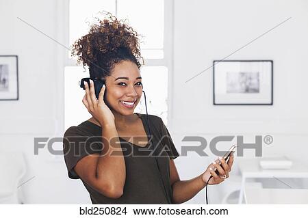 Picture - Mixed race woman listening to cell phone with headphones. Fotosearch