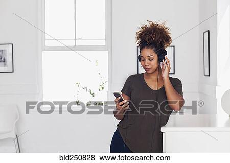 Stock Photo - Mixed race woman listening to cell phone with headphones. Fotosearch