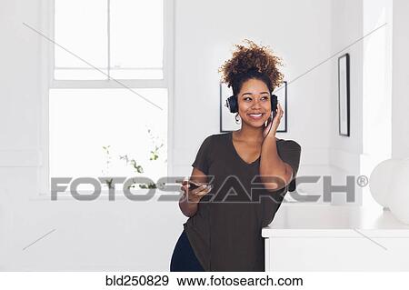 Stock Photo - Mixed race woman listening to cell phone with headphones. Fotosearch