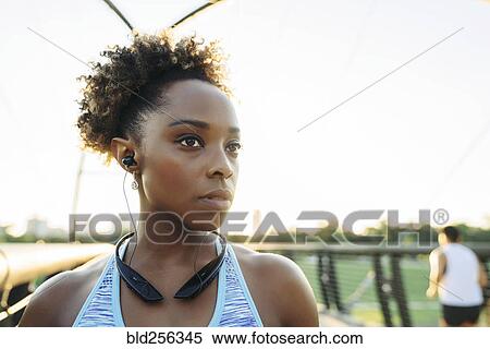 Stock Photography - Mixed Race woman listening to earbuds on bridge. Fotosearch