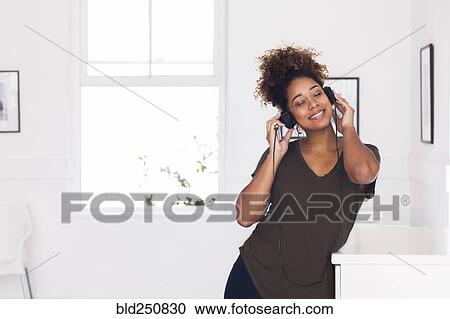 Stock Image - Mixed race woman listening to headphones. Fotosearch