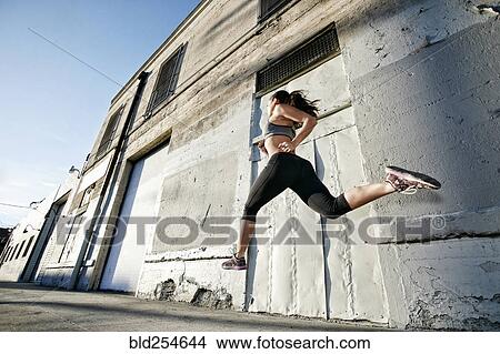 Picture - Mixed race woman running and jumping on sidewalk. Fotosearch