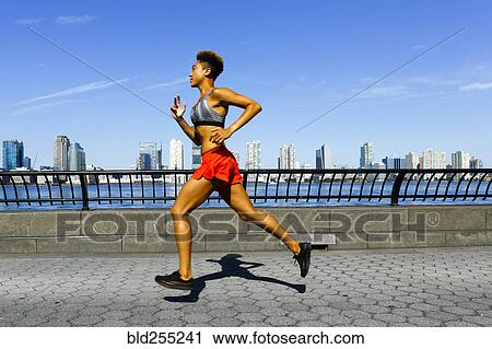 Stock Image - Mixed race woman running at waterfront. Fotosearch