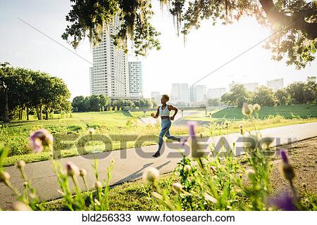 Stock Image - Mixed Race woman running on path in park beyond wildflowers. Fotosearch