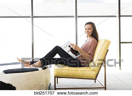 Stock Photo - Mixed race woman sitting on chair reading book. Fotosearch