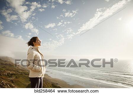 Mixed Race woman standing on beach admiring ocean View Large Photo Image Picture - Mixed Race woman standing on beach admiring ocean. Fotosearch