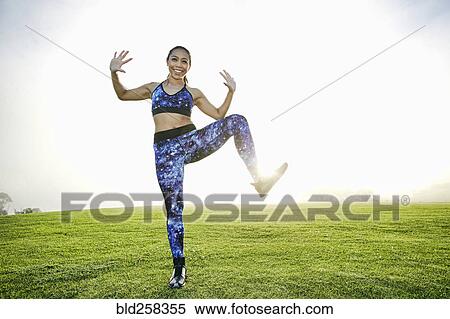 Stock Photography - Mixed race woman standing on one leg in field. Fotosearch