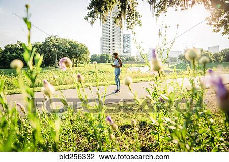 Stock Image - Mixed Race woman standing on running path in park beyond wildflowers. Fotosearch