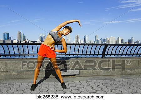 Stock Photo - Mixed race woman stretching arm at waterfront. Fotosearch
