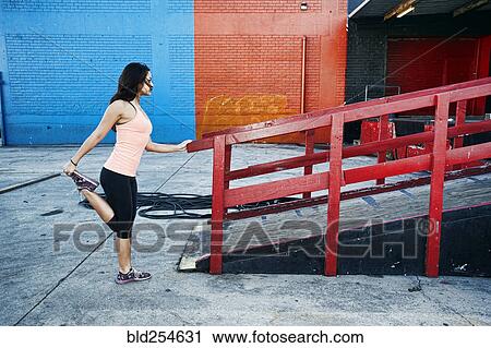 Stock Image - Mixed race woman stretching leg at loading dock. Fotosearch