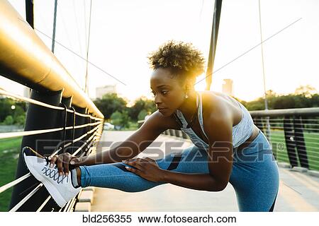Stock Photography - Mixed race woman stretching leg on bridge railing. Fotosearch