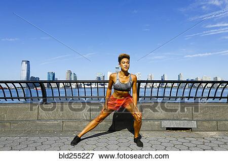 Stock Photo - Mixed race woman stretching legs at waterfront. Fotosearch