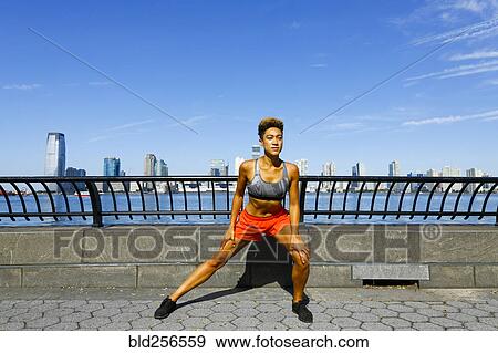 Stock Photo - Mixed race woman stretching legs at waterfront. Fotosearch