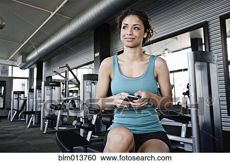 Stock Image - Mixed race woman text messaging on cell phone in health club. Fotosearch