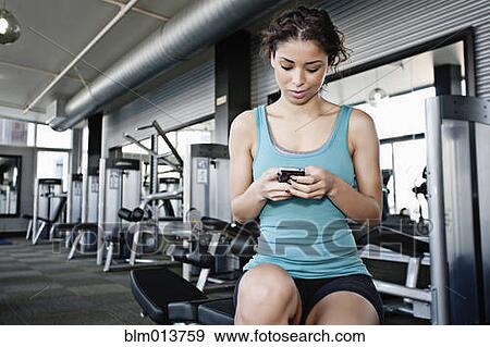 Stock Photo - Mixed race woman text messaging on cell phone in health club. Fotosearch