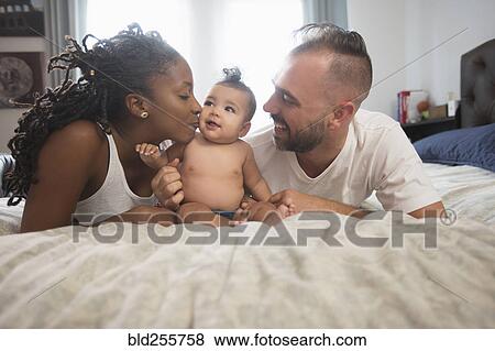 Mother and father laying on bed with baby daughter View Large Photo Image Stock Photo - Mother and father laying on bed with baby daughter. Fotosearch