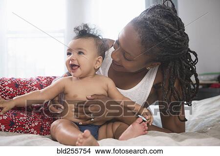 Picture - Mother holding smiling baby daughter on bed. Fotosearch